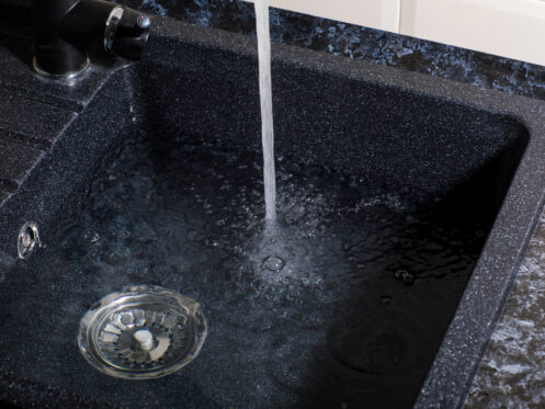 A kitchen sink has water filling it up. The drain is plugged by a drain cover to prevent the water from escaping.