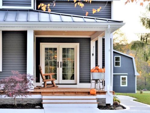 A cozy porch with a wooden rocking chair beside some fall decor. Autumn leaves and warm light enhance the welcoming, seasonal atmosphere.